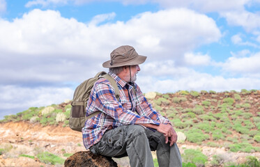 Portrait of a senior bearded man carrying a backpack while resting looking at the mountain and smiling. Fit old man on a hiking trip enjoying adventure freedom and healthy vacation