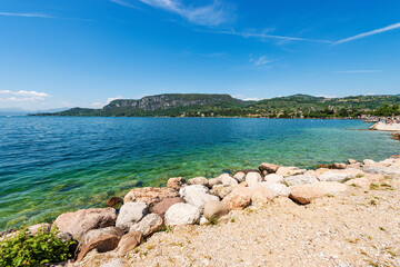 Beach and bay of water in front of Garda town, tourist resort on the coast of Lake Garda (Lago di Garda). Verona province, Veneto, Italy, Europe. On horizon the headland or promontory of San Vigilio.