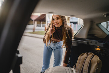 One young beautiful woman receiving bad news while talking on mobile phone forgot to take important luggage baggage or other stuff while unpacking from the back of car taking belongings call for help