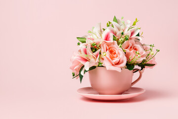 Tea cup filled with bouquet of fresh roses and orchids on pastel pink background. Creative floral spring bloom concept. Morning drink or healthy breakfast idea. Still life natural visual trend.