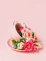 Tea cup and plate with bouquet of fresh roses and orchids on pastel pink background. Creative...