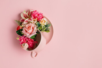 Teacup and plate with bouquet of fresh flowers on pastel pink background. Creative floral spring...