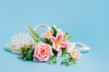 Bouquet of pink rose and orchid flowers in a shopping crochet bag on pastel blue background. Creative floral spring bloom concept. Flower delivery idea. Still life natural visual trend.