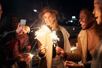 Nightlife in the city, young adult group of Multi-cultural friends at a rooftop party lighting sparklers. Taking photos for social media