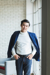 Studio shot Asian young thoughtful handsome successful professional male businessman in casual blue suit turtle neck shirt standing  thinking on brick wall look at camera