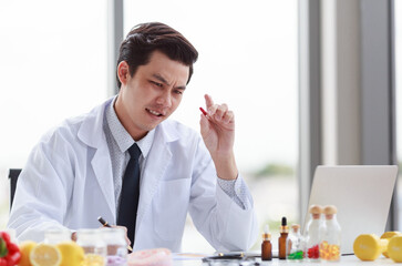 Portrait studio shot Asian male professional nutritionist dietitian doctor in white lab coat and stethoscope sitting holding pen smiling at working desk full of fruits vegetable nutrition supplements