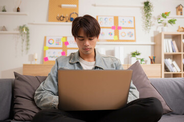 Naklejka premium At home, a business asian man types and works online on a desk table with a laptop.