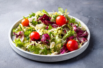 Plate with mix of fresh green leaves and tomatoes on a grey background. Healthy food eating and diet concept