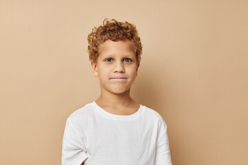 Cheerful boy with curly hair in a white t-shirt beige background