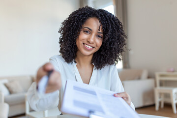 Sign Here. Young smiling confident woman pointing to a contract, sheet of paper, holding a pen, looking and showing it at camera. Presentation, Agreement, Business Concept. - obrazy, fototapety, plakaty
