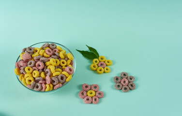 A bowl of breakfast cereal on a turquoise background, decorated with flowers from cereal rings with leaves.