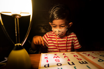 A boy wearing a safety mask is sitting at home reading an English alphabet learning book. Asian boy...