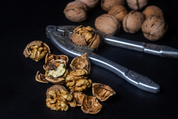 Chopped walnuts on a black background. A steel nutcracker cracks nuts. broken nuts