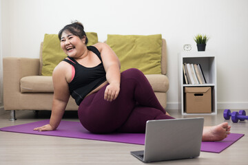 Fototapeta na wymiar Young asian sport woman plus size sitting practicing yoga lesson. Stretching training workout on yoga mat at home for good health and body shape.