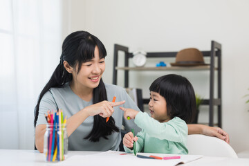 Happy asian boy painting with crayon and colored pencil with his mother in living room at home. Mom teaching son how to painting with crayon color on book or doing homework. family concept.