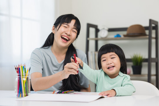 Mom teaching son how to painting with crayon color on book or doing homework. Happy asian boy painting with crayon and colored pencil with his mother in living room at home.  family concept.
