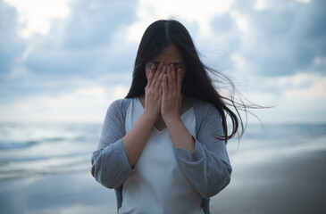 A sad and stressed Asian woman stands alone on the beach in the evening. Dramatic atmosphere. disappointment in life. She stood crying alone