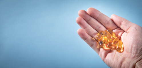 Male hand showing fish oil Omega 3 capsules on the blue background.