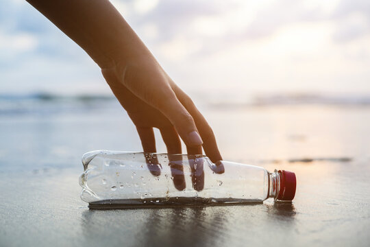 Close up woman hand pick up the plastic bottle on the beach. Female Volunteer clean the trash on the beach make the sea beautiful. World environment day concept.