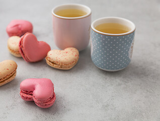 Macarons or French macaroons in heart shapes and two cups on gray background with copy space