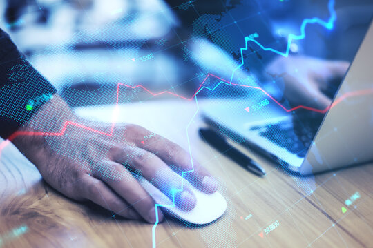 Close up of businessman hands using laptop keyboard and mouse on wooden desktop with creative glowing blue map hologram with chart and grid on blurry background. Economy, world and stock concept.