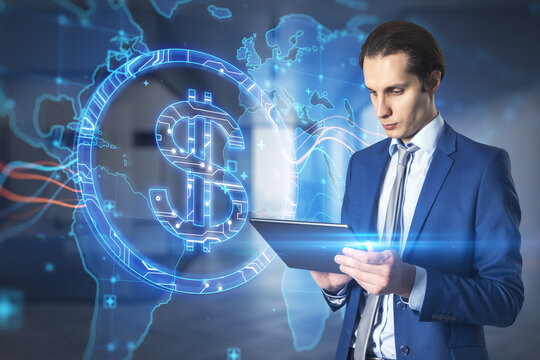 Attractive young european businessman using tablet with abstract glowing blue dollar sign and map with charts on blurry office interior background. Currency, trade and digital market concept. 