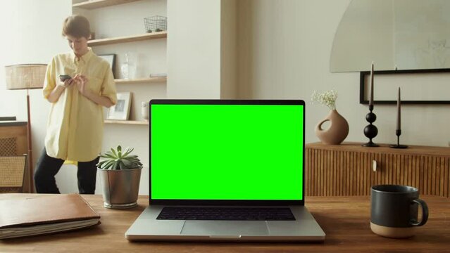 An open laptop with a green screen standing on a table in a home interior