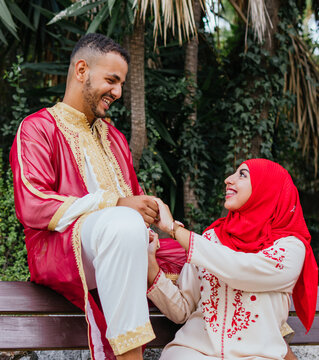 shot of a lovely couple of an arab country sitting on a bench of a public park while look each other and hold their hands