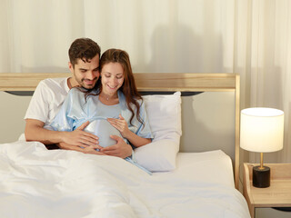 Cheerful husband enjoy embracing pregnant wife and happy to tenderly fondle beloved belly of unborn baby and expecting warm family during prenatal care of maternity at romantic bedroom