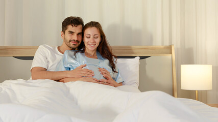 Cheerful husband enjoy embracing pregnant wife and happy to tenderly fondle beloved belly of unborn baby and expecting warm family during prenatal care of maternity at romantic bedroom