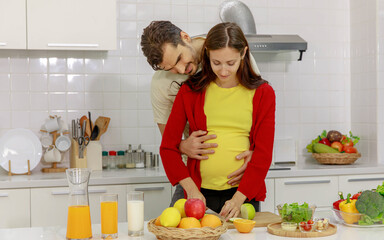 Cheerful husband joyfully embracing happy pregnant wife from behind with sweet love. Romantic couples tenderly hug beloved belly of unborn baby as warm care for maternity in kitchen room