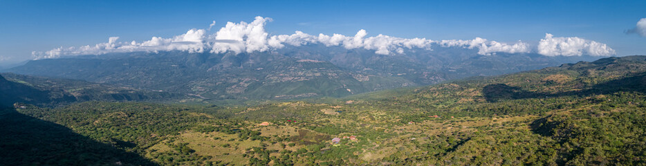 Fototapeta na wymiar Panoramic aerial view from the plateau to the valley and adjacent mountains covered with white clouds, blue Sky, Barichara, Colombia
