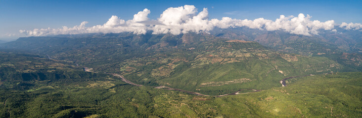 Naklejka premium Panoramic aerial view from the plateau to the valley and adjacent mountains covered with white clouds, blue Sky, Barichara, Colombia
