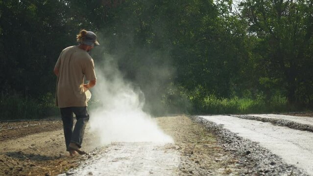 Farmer spreading white organic fertilizer un the furrows of a farming fiel, barefoot rural worker