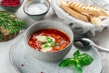 Italian vegetable soup with tomatoes, basil, cheese and vegetables in a gray bowl. Tomato cream soup served on table