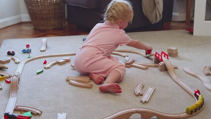 Young girl at home playing with wooden train set toy on carpet - shot in slow motion