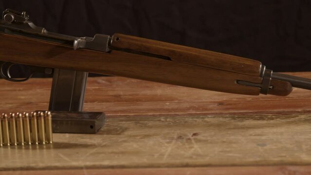 Wide Dolly of classic 30m1 carbine rifle with ammunition on the foreground standing on a wooden surface
