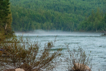 fog over the water of a mountain river on the background of a forest and a mountain