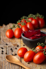 Top view of cherry tomatoes, bowl with beets, spoon and peppercorns, on rustic wooden table, selective focus, black background, vertical