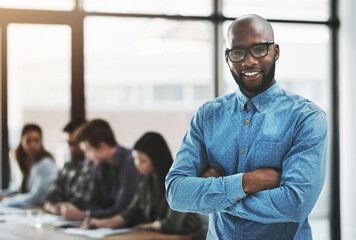 Were always ready to help you succeed. Portrait of a cheerful businessman posing with his arms folded in a modern office with his colleagues in the background.