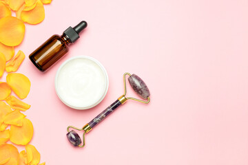Face roller with cosmetic serum, face cream on a pink background and rose petals. Skincare, natural organic cosmetics concept. Top view, flat lay.