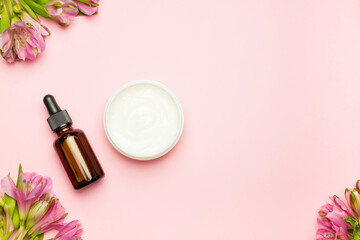 Obraz na płótnie Canvas Cosmetic serum, face cream on a pink background and flowers. Skin care, the concept of natural organic cosmetics. Top view, flat position.