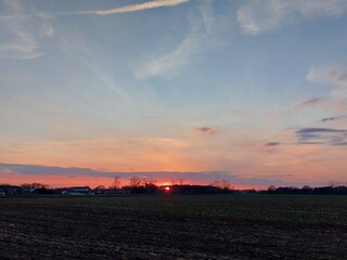 Dämmerung auf einer Agrarlandschaft. Der Himmel wird dunkel. Die Sonnenuntergänge im Westen mit Rötung. Der Mond erscheint am Himmel über der Wiese. Der Wald verwandelt sich in Silhouetten. Abend.
