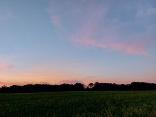 Sonnenuntergang, gefolgt von bunten Wolken. Der Himmel über den schlafenden Feldern und Bäumen. Die Natur malt den Himmel und löscht ihn aus. Romantische Szenen für Hintergründe. Dämmerung in Rottönen
