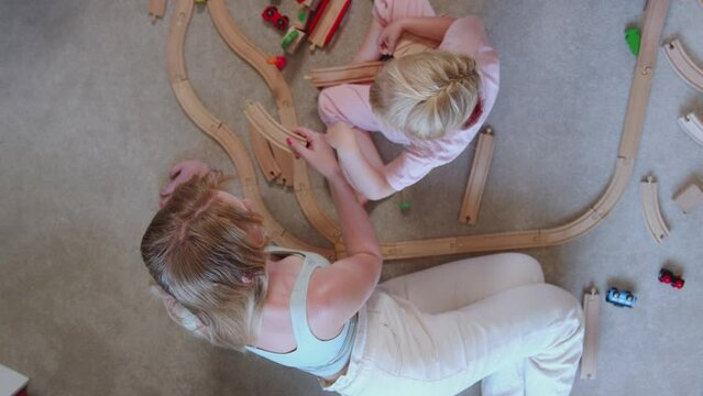 Overhead shot of Mother and daughter at home playing with wooden train set toy on carpet - shot in slow motion