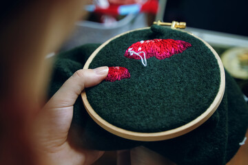 Embroidery process with cotton thread of mushrooms hat. Woman's hands sewing on green cloth. Needlework concept. Craft and handmade.