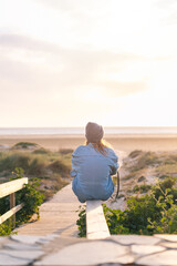Fototapeta na wymiar vertical photo of an unrecognizable young woman sitting by the beach enjoying a sunset
