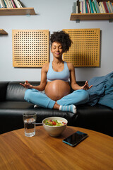 Healthy pregnant woman doing breathing and relaxation yoga exercise sitting on her sofa at home