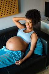 Portrait of cheerful black young pregnant woman resting at home in her couch.