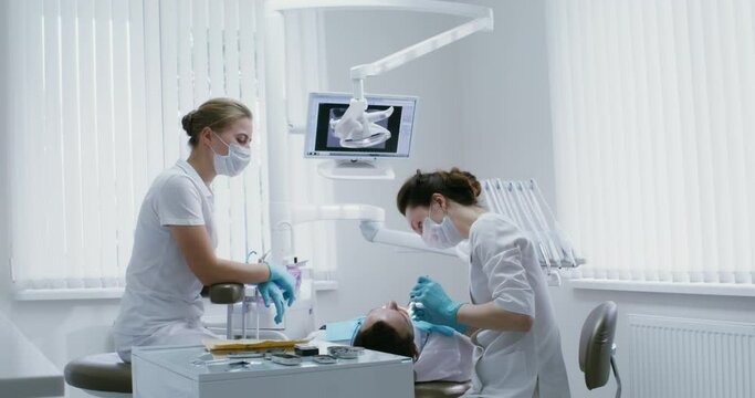 A female dentist examines the oral cavity of a patient lying on a dental chair